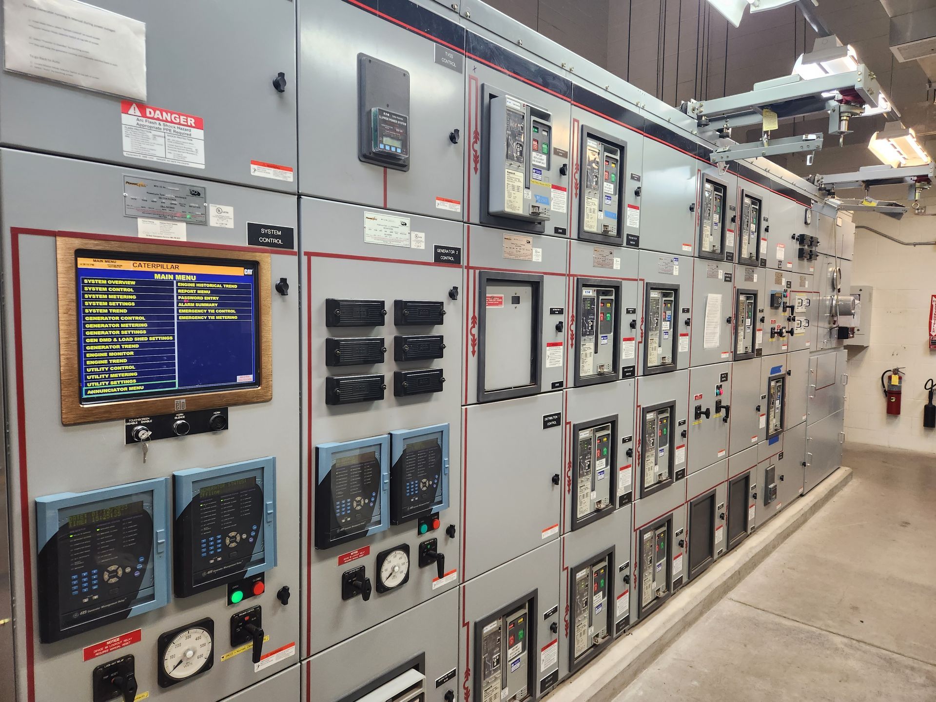 A row of electrical panels with a monitor on the wall.