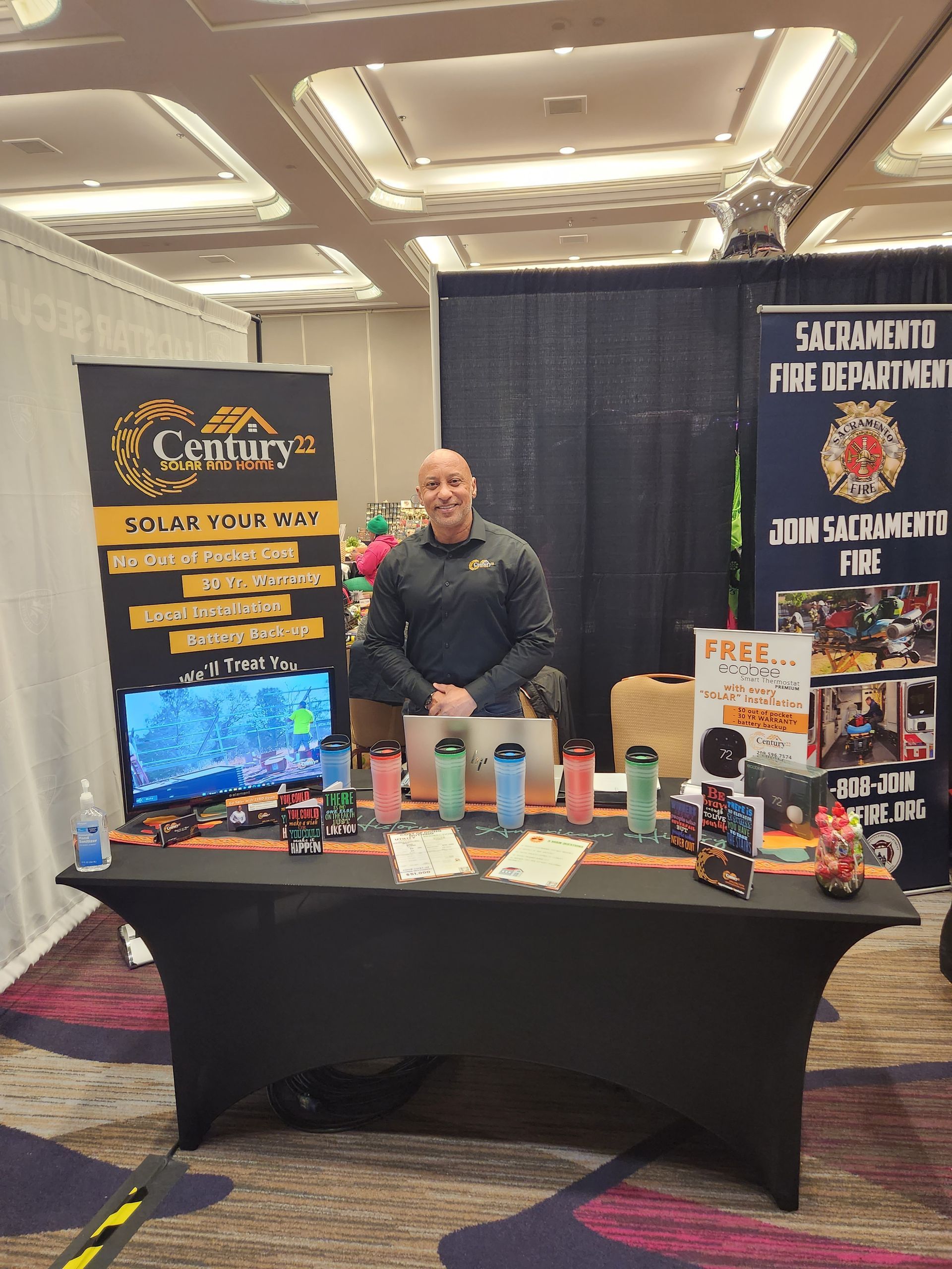 A man is standing behind a table at a convention.