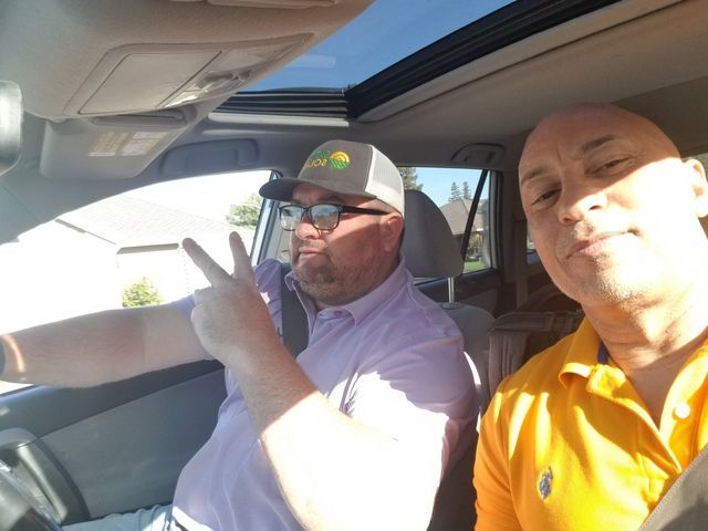 Two men are sitting in a car and one of them is wearing an orange polo shirt