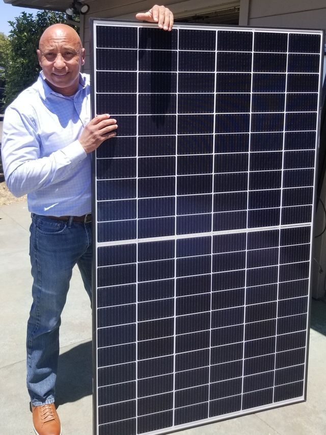 A man is holding a large solar panel in his hands.
