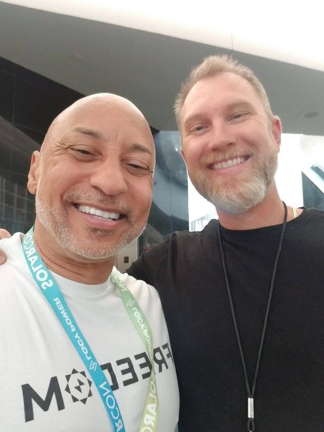 Two men are posing for a picture and one has a lanyard around his neck that says major