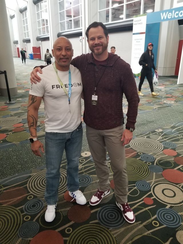 Two men are posing for a picture in front of a welcom sign