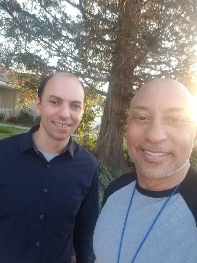 Two men are posing for a picture in front of a tree.