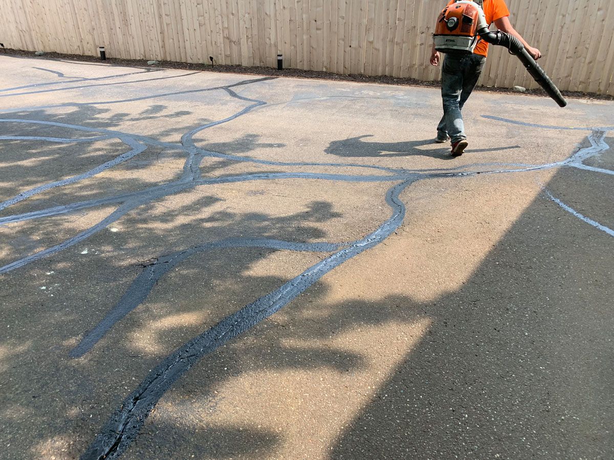 A man is walking down a concrete driveway with a blower.