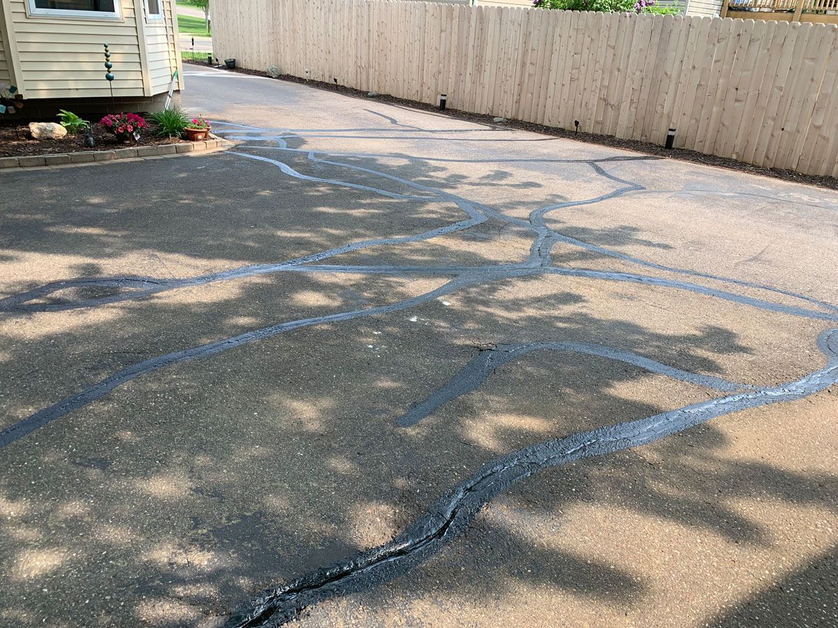 A cracked asphalt driveway with a wooden fence in the background.