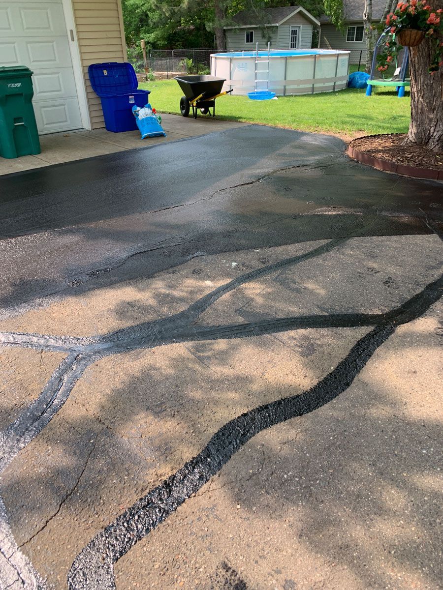 A driveway with a pool in the background and a wheelbarrow in the foreground.
