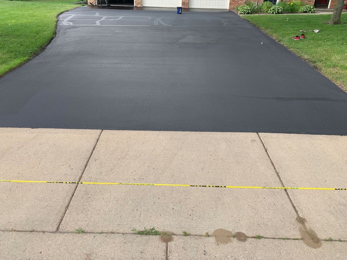 A black driveway with a yellow line on the sidewalk in front of a house.