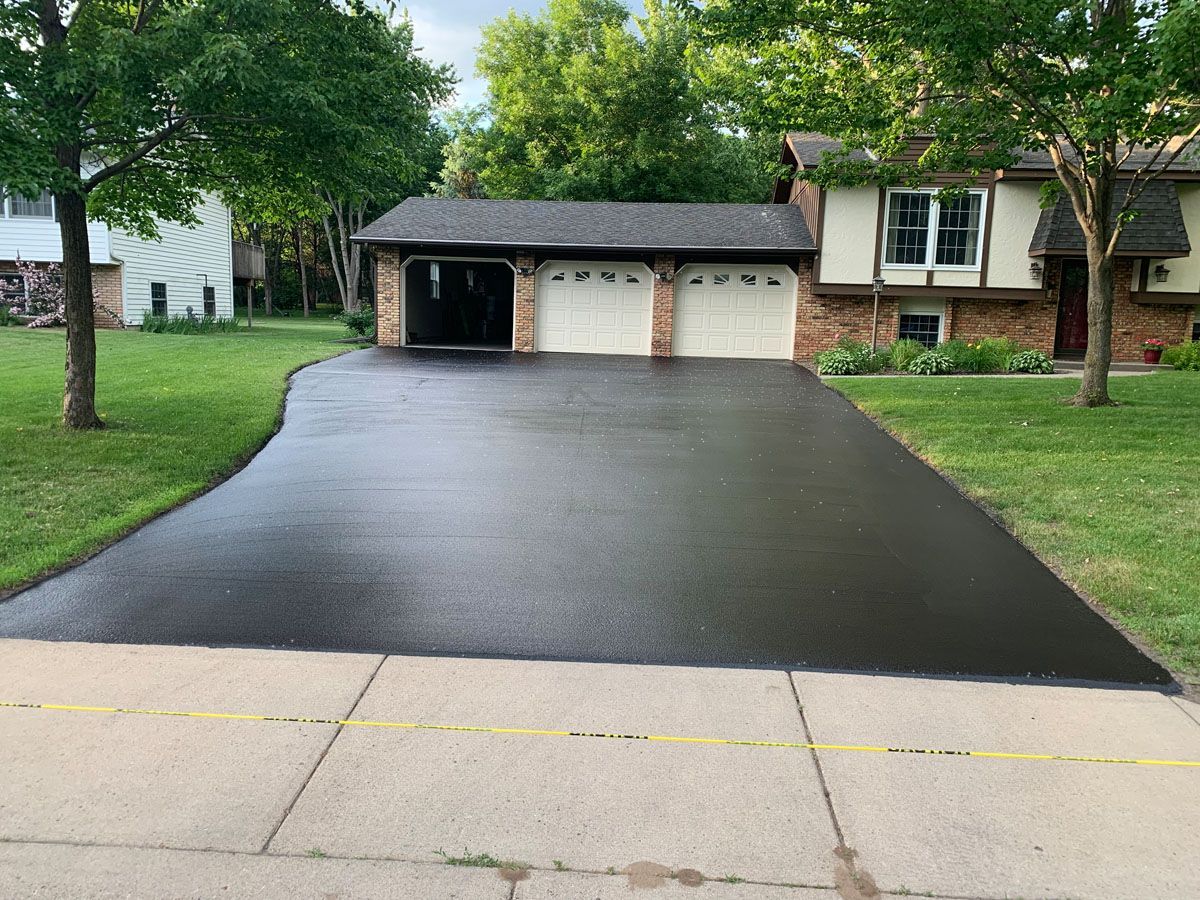 A black driveway leading to a house with two garage doors.