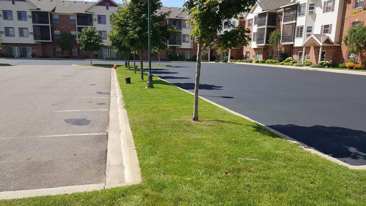 A parking lot next to a building with a lot of grass and trees.
