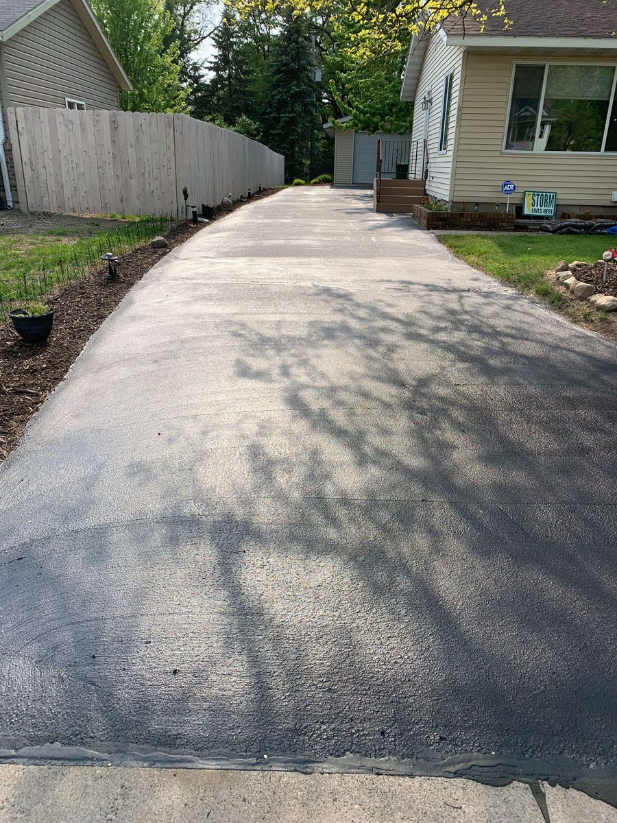 A concrete driveway leading to a house with a wooden fence.