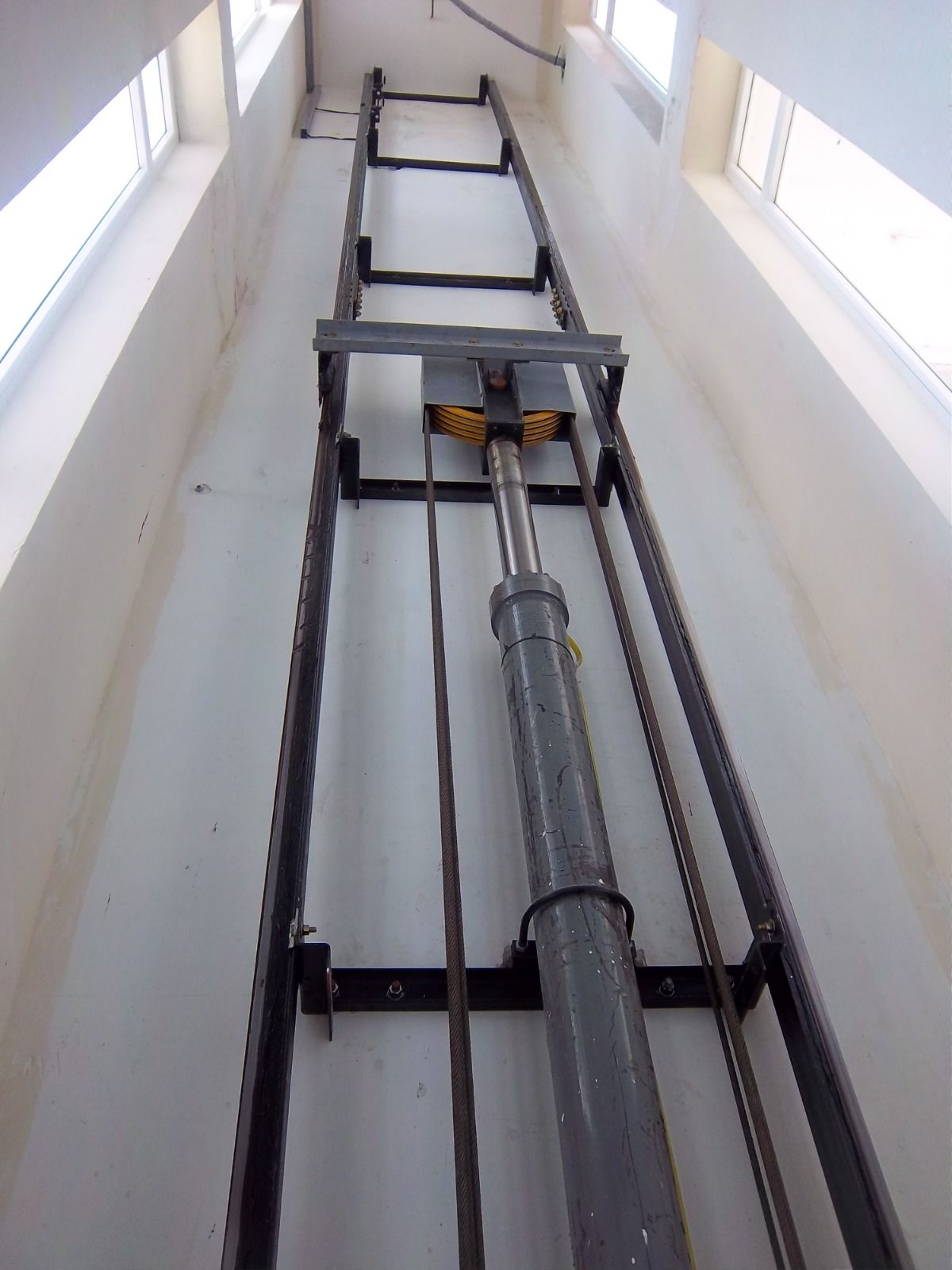 Mecanismo de elevación hidráulico dentro de un eje largo y estrecho con marco de metal, cables y un cilindro hidráulico.