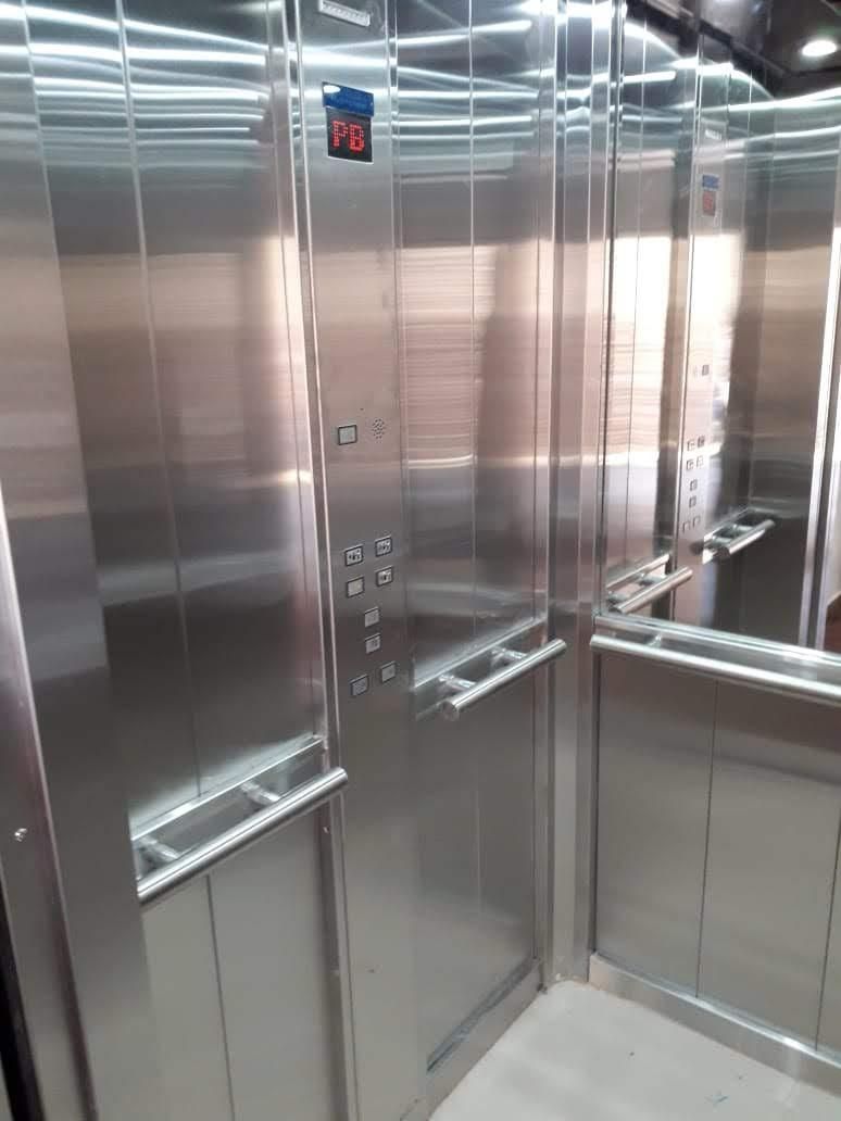 Interior de un ascensor con paredes de acero inoxidable, botones y barras de apoyo. El piso muestra el número 6.