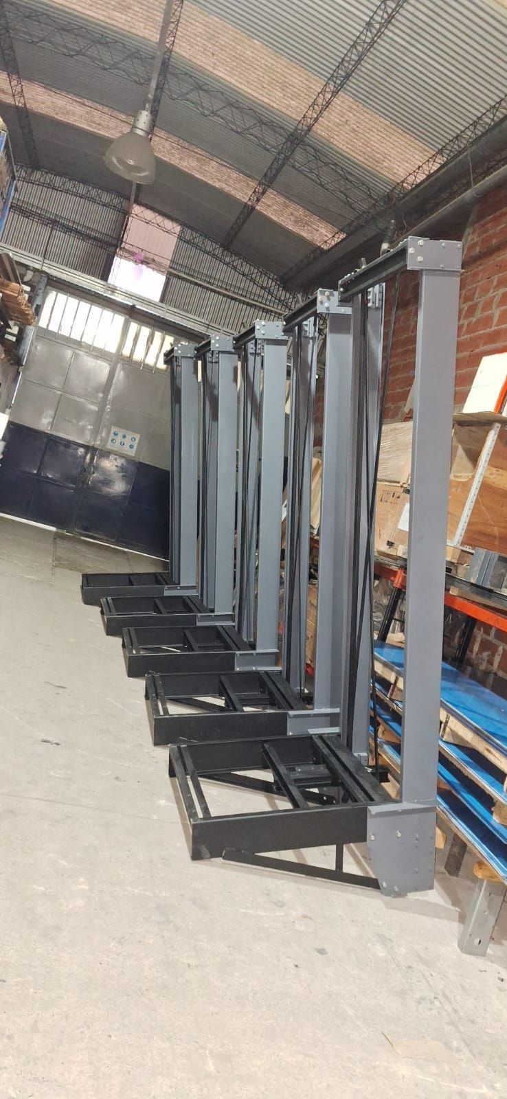 Componentes de un elevador industrial gris alineados dentro de un almacén.