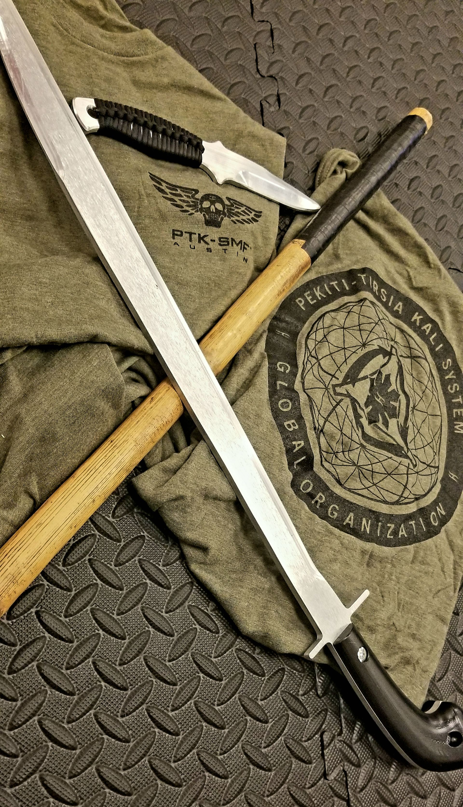 A sword and knife set arranged over a cloth bag. Both are on a black rubber patterned surface.