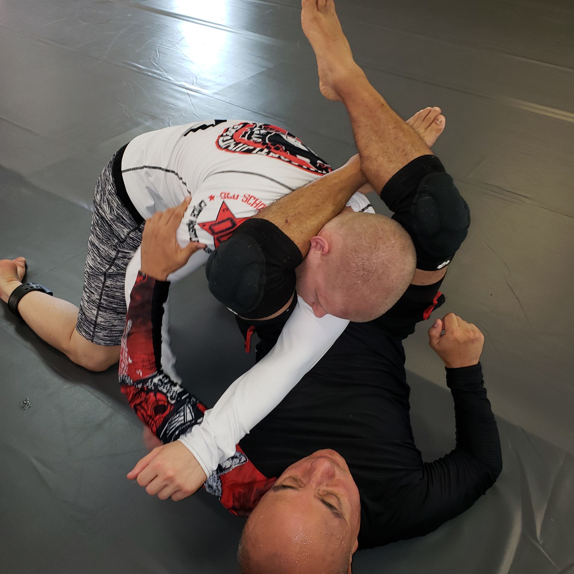 Two men grappling on a mat, one in a white rash guard is applying a choke.