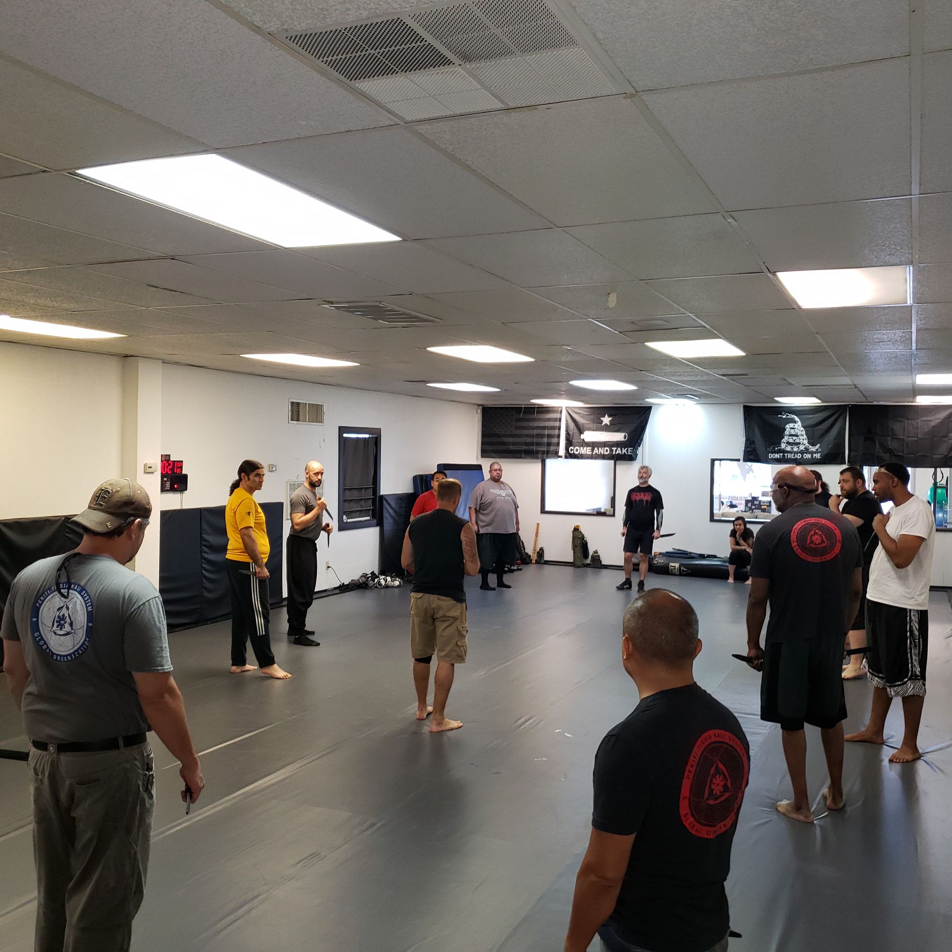 People in a martial arts class, standing on a mat in a gym.
