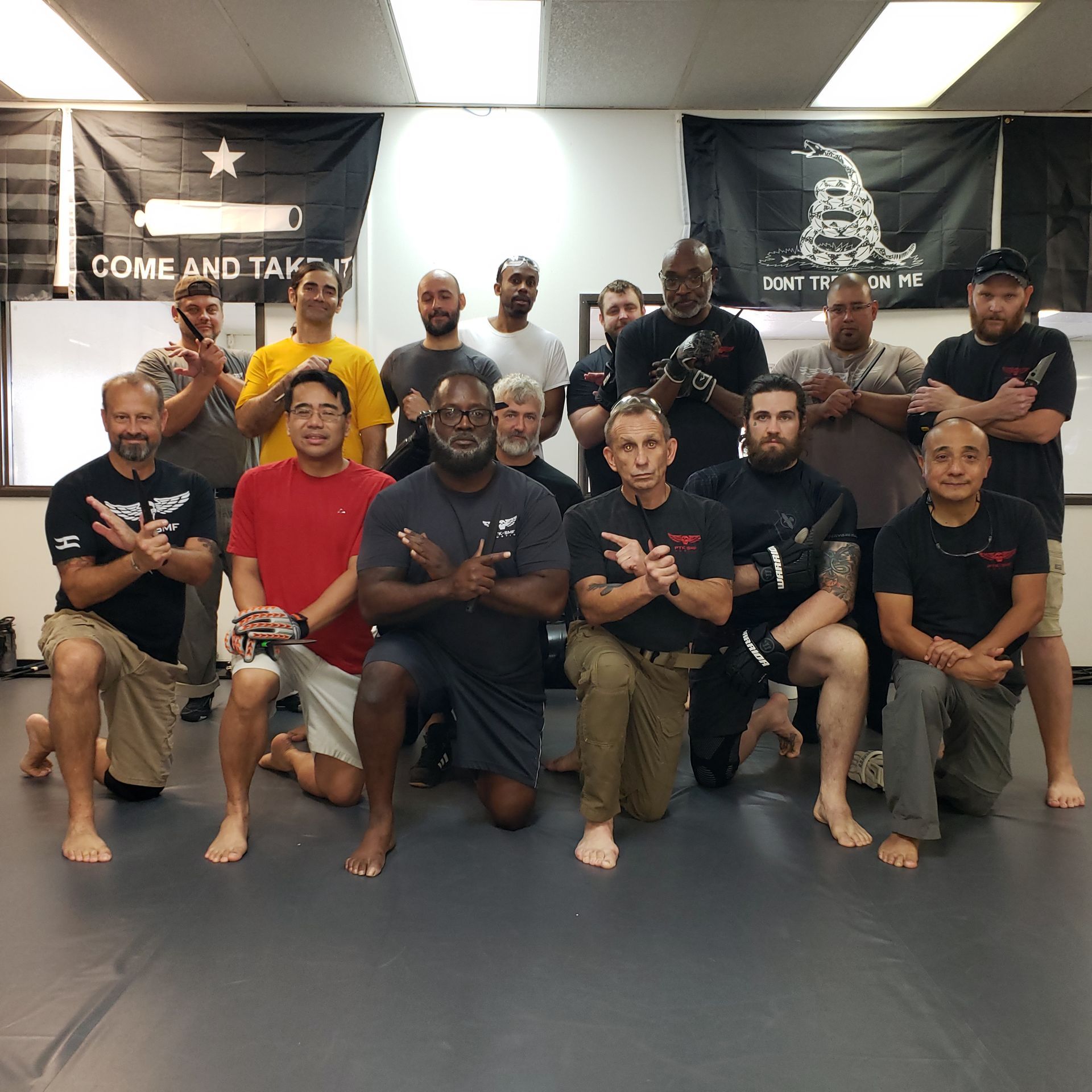 Group of people in a training room. Some kneeling, hands in front. Flags and a whiteboard are visible.