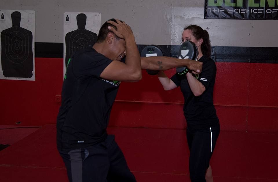 Man practicing a punch, guarding his head, while woman holds a mitt. Training in a gym.