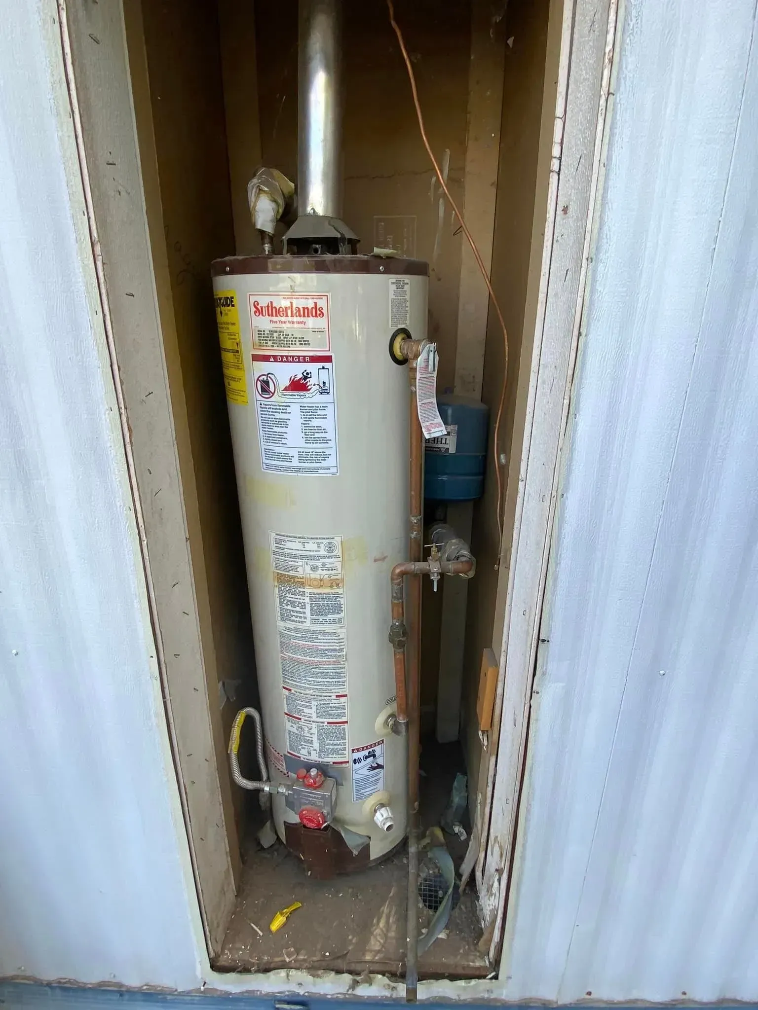 Water heater in a recessed alcove; beige tank, silver vent, copper pipes.