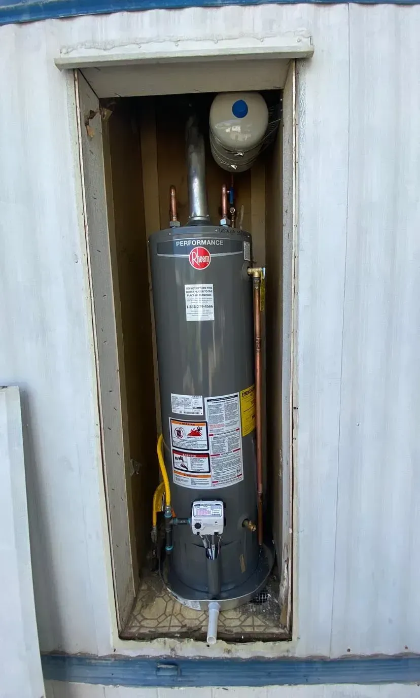 A tall, gray Rheem water heater installed in a recessed alcove. A blue expansion tank sits above it.