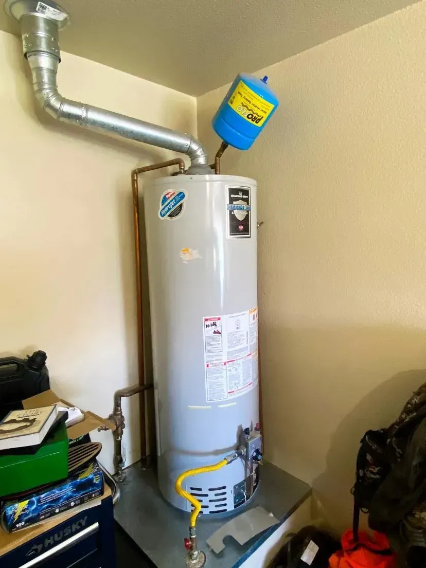 A tall, cylindrical water heater in a corner, with a blue expansion tank and metal vent pipe.