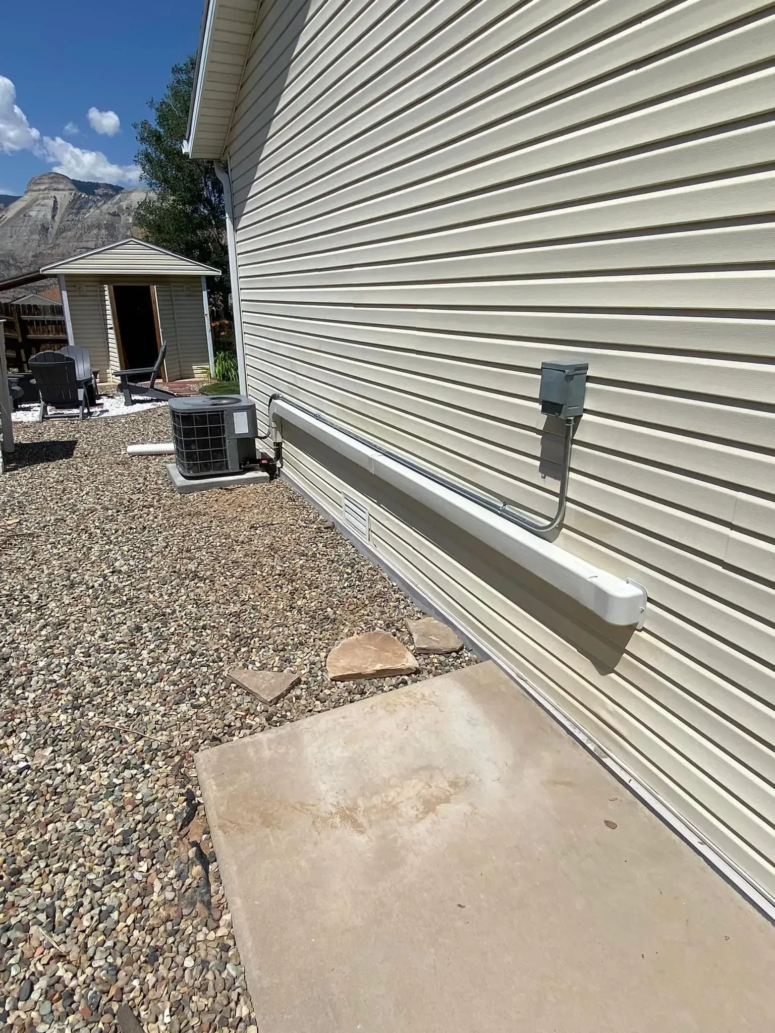 Side of beige house with gravel, concrete, and air conditioning unit.