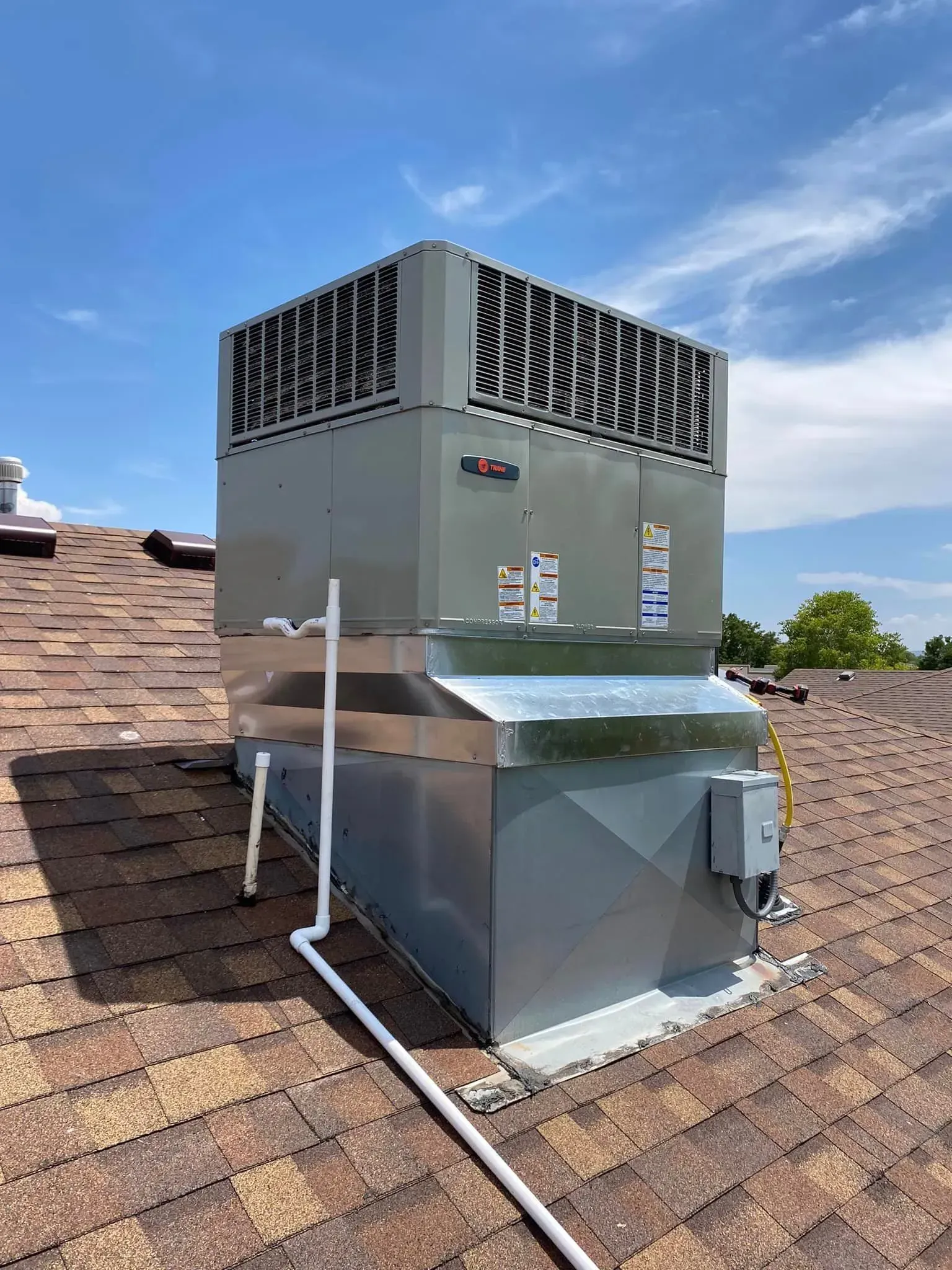 Rooftop HVAC unit on brown shingle roof against a blue sky.