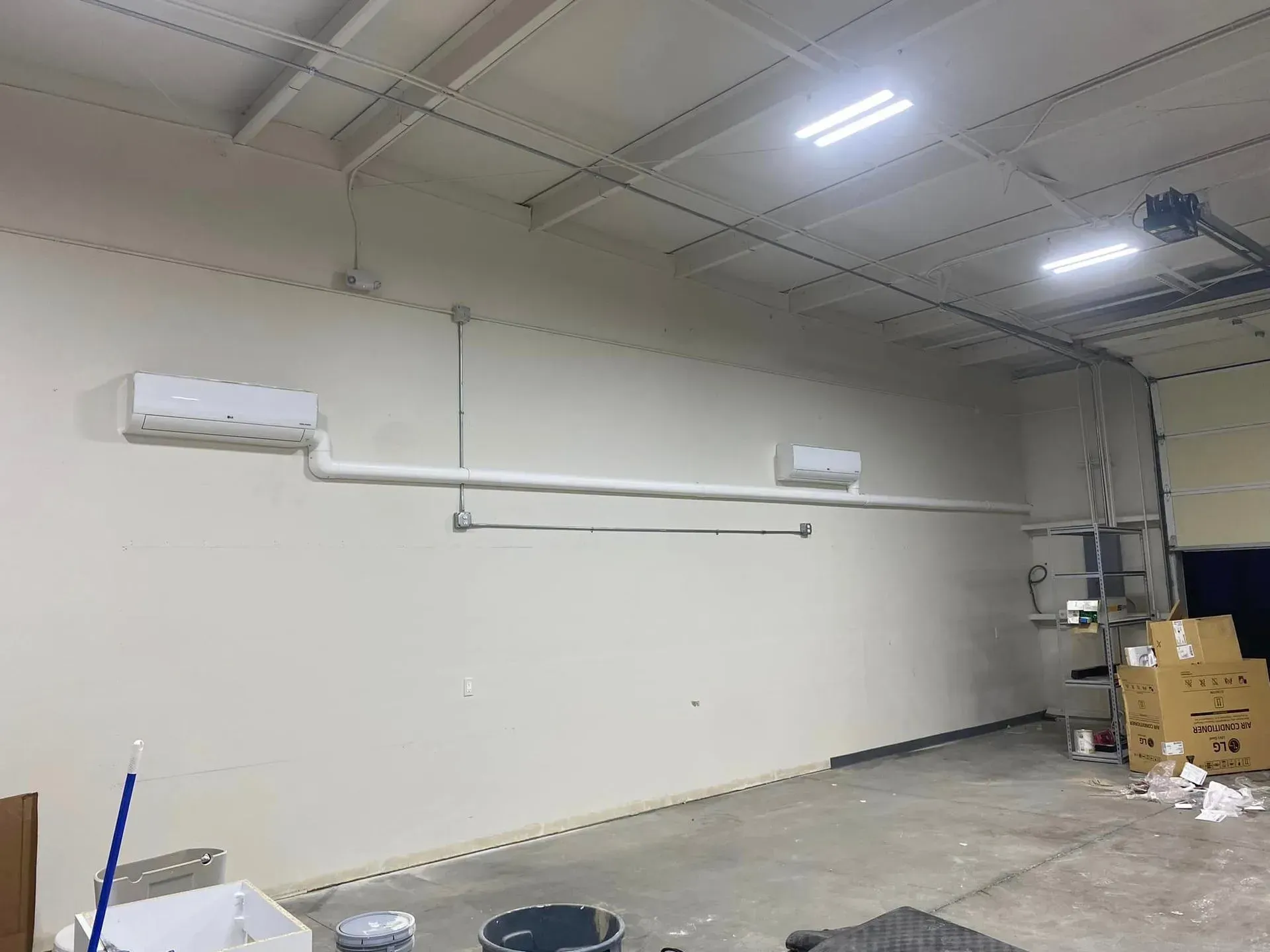 A white-walled industrial interior with two mounted AC units and pipes running along the wall.
