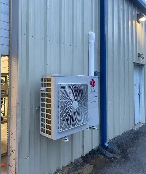 LG air conditioner unit mounted on a gray metal building exterior wall with white vent pipe.