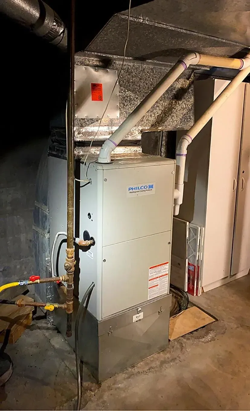 A furnace unit with white pipes and gas lines in a basement setting.