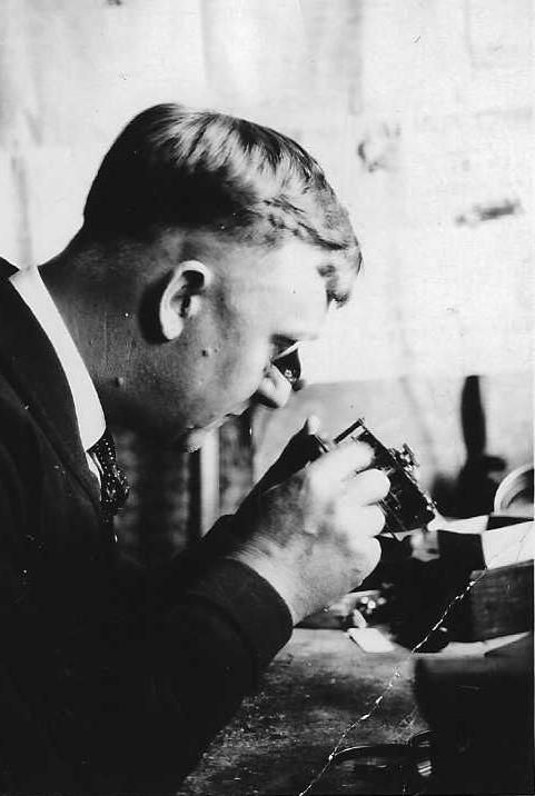 Man examining object up close, likely with jewelry tools, in workshop setting.