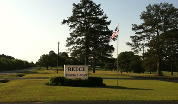 A sign for reece funeral home is in the middle of a grassy field