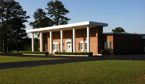 A brick building with white columns and a driveway in front of it