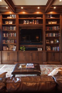 Built-in wooden bookcase with TV, books, and photos; leather couch and ottoman in a living room.