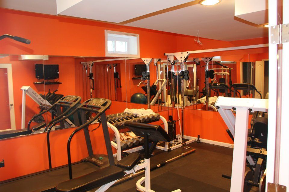 Home gym with orange walls, various exercise machines, and a large mirror.