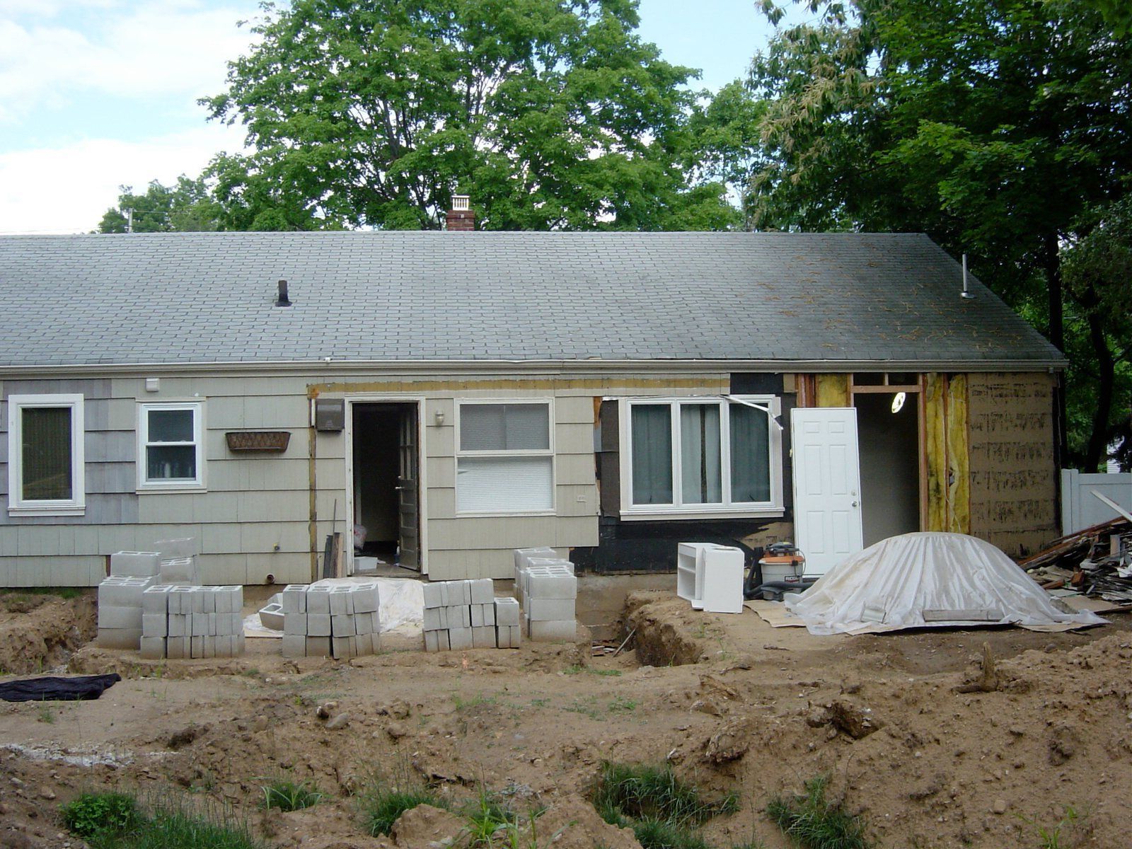 House undergoing renovations; gray siding, exposed framing, cement blocks on dirt.