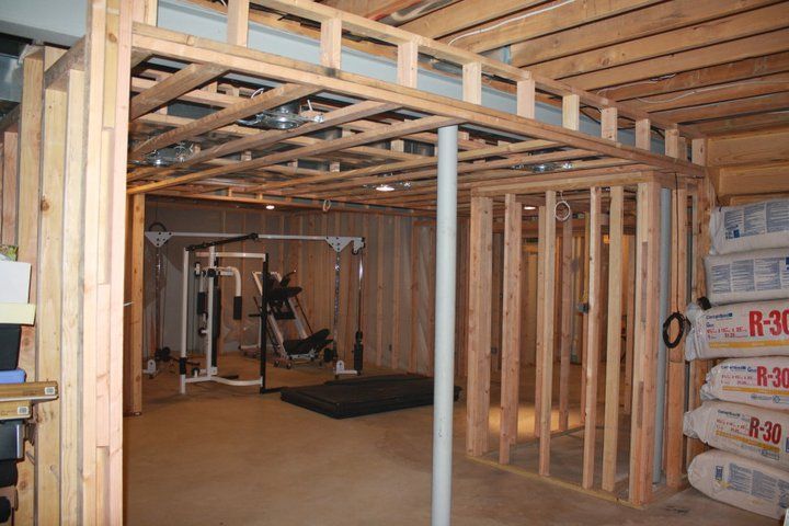 Framed wooden walls in a basement under construction; exercise equipment in the background.