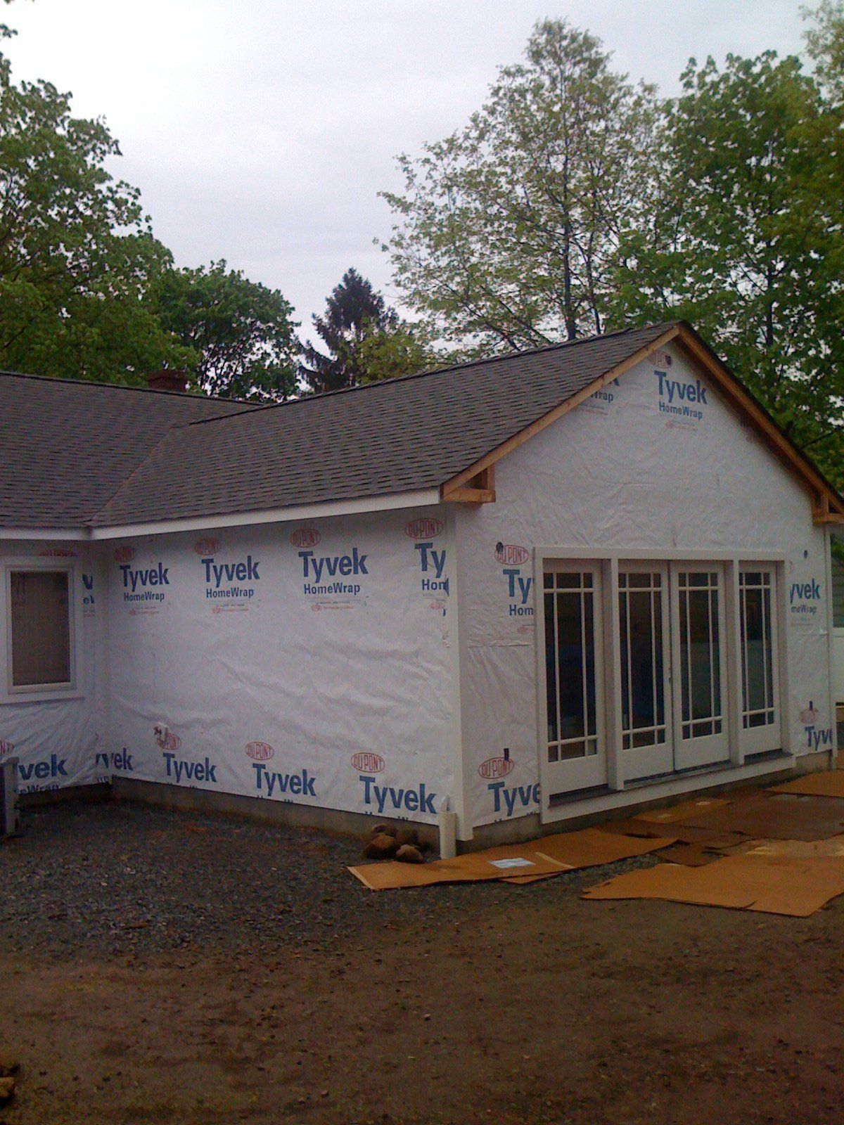 House exterior under construction, covered in Tyvek, with new doors and windows installed.