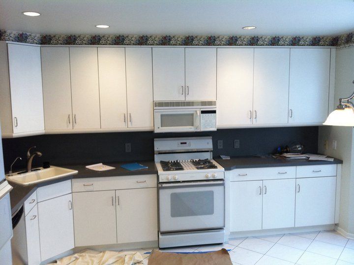White kitchen cabinets with a microwave, stove, and sink against a dark blue backsplash.