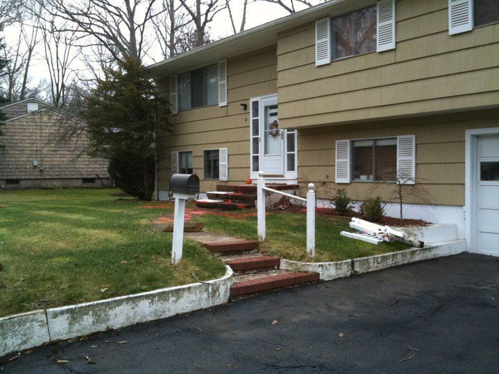 Two-story tan house with white trim, steps to the front door, and a driveway.