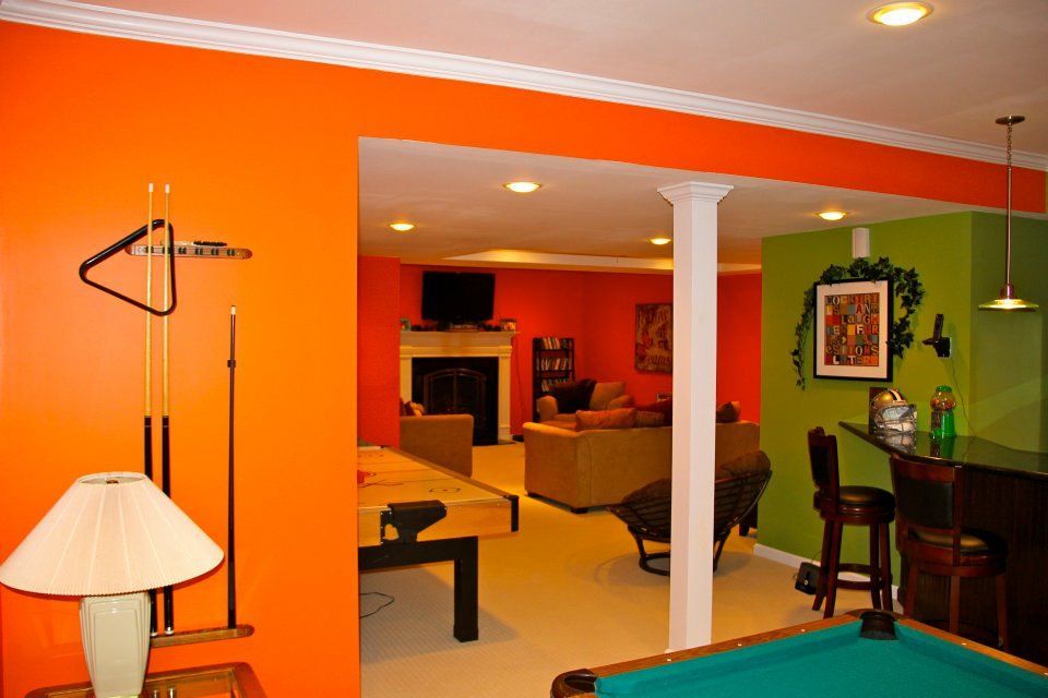 Basement game room with orange walls, pool table, fireplace, and bar with green accent wall.