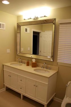 Bathroom with double vanity, large mirror, beige walls, and white cabinet.