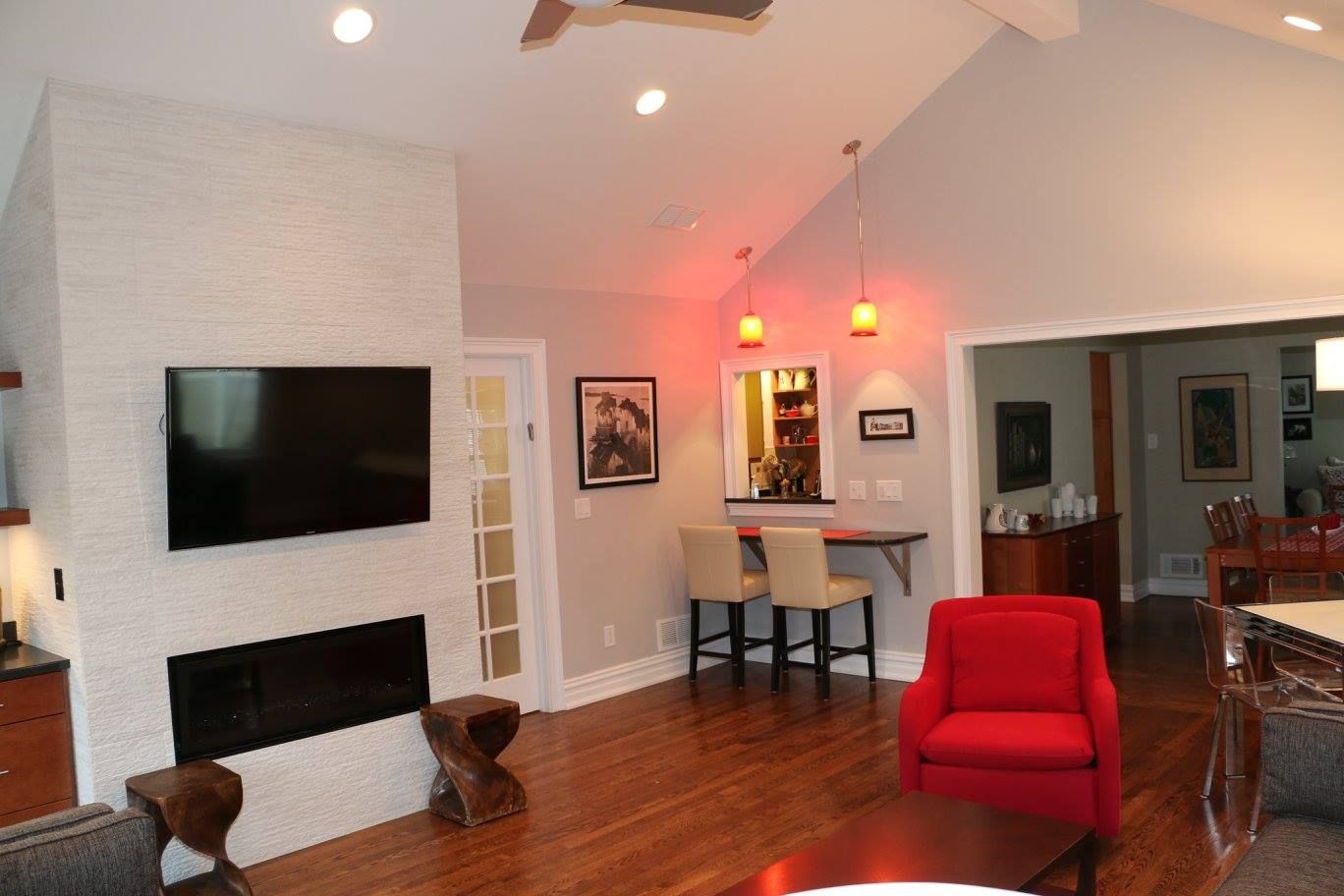 Living room with brick fireplace, TV, bar area, red chair, and wooden floor.