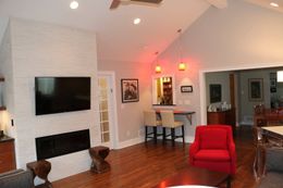Living room with brick fireplace, TV, bar area, red chair, and wooden floor.