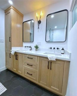 Bathroom with light wood vanity, black hexagon tile floor, two mirrors, and black fixtures.