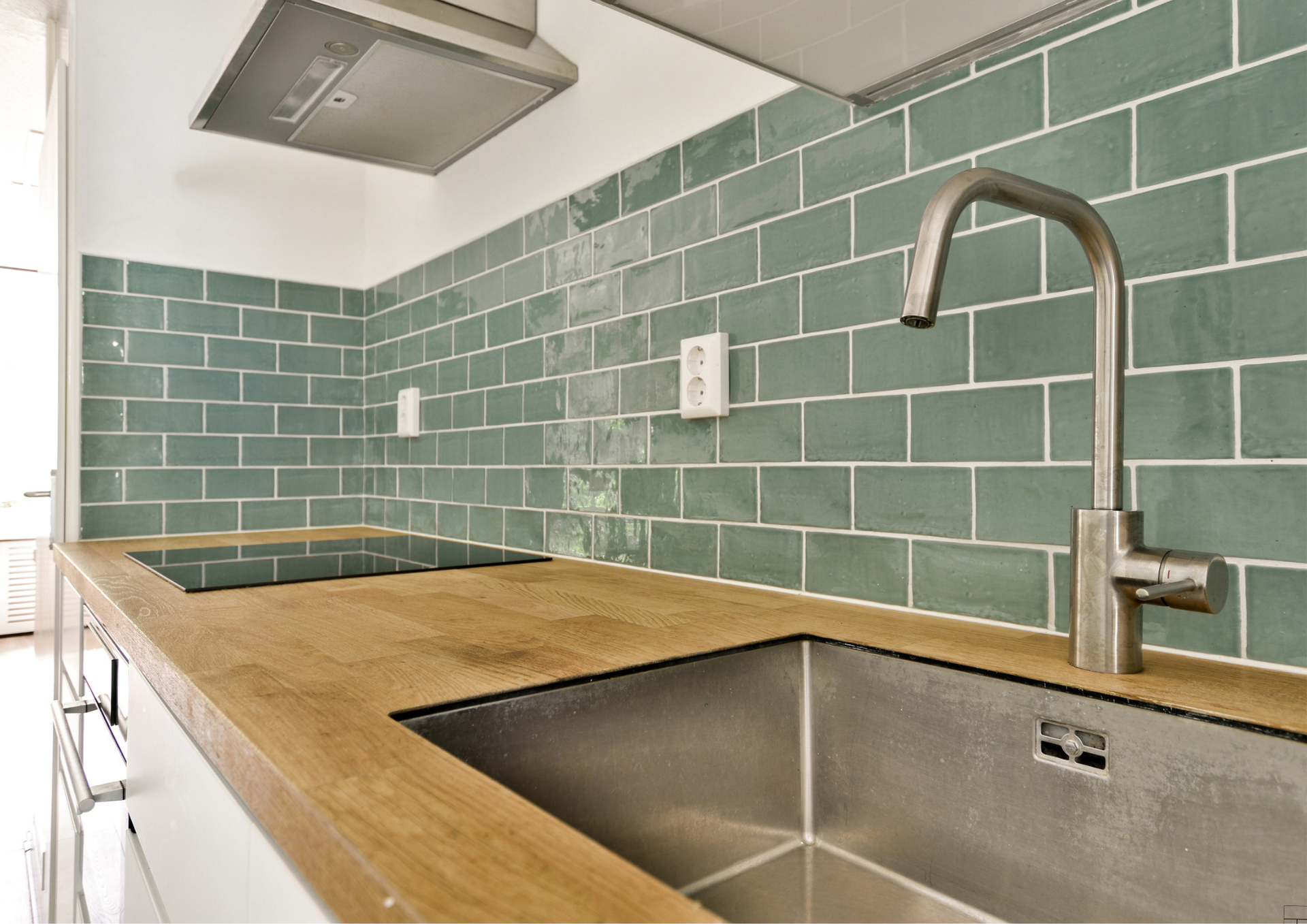 Kitchen with wooden countertop, stainless steel sink and faucet, teal tiled backsplash.