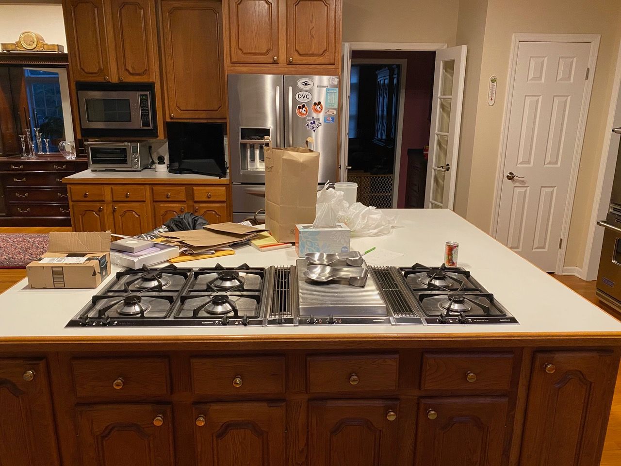 Kitchen island with stovetop, cluttered with boxes and a paper bag; wooden cabinets in the background.