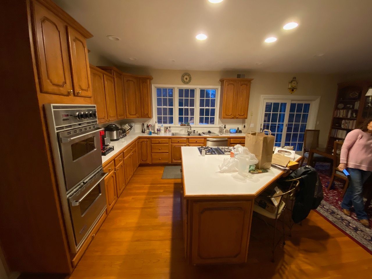 Kitchen with wooden cabinets, island, and stainless steel oven. Person in pink shirt is visible.
