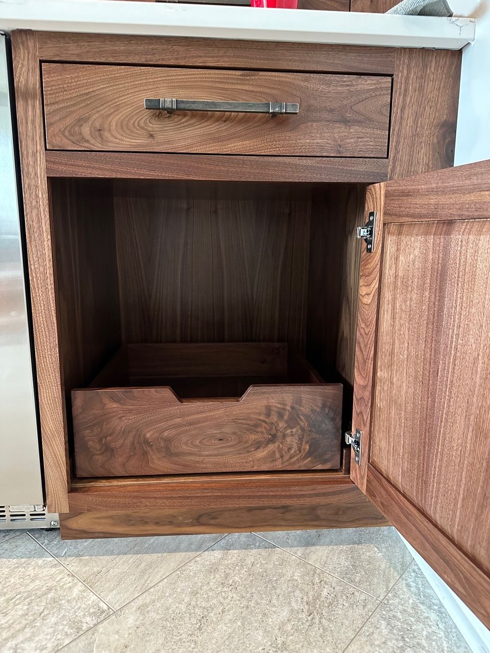 Open wooden kitchen cabinet with drawer and a pull-out tray. Brown stained wood.