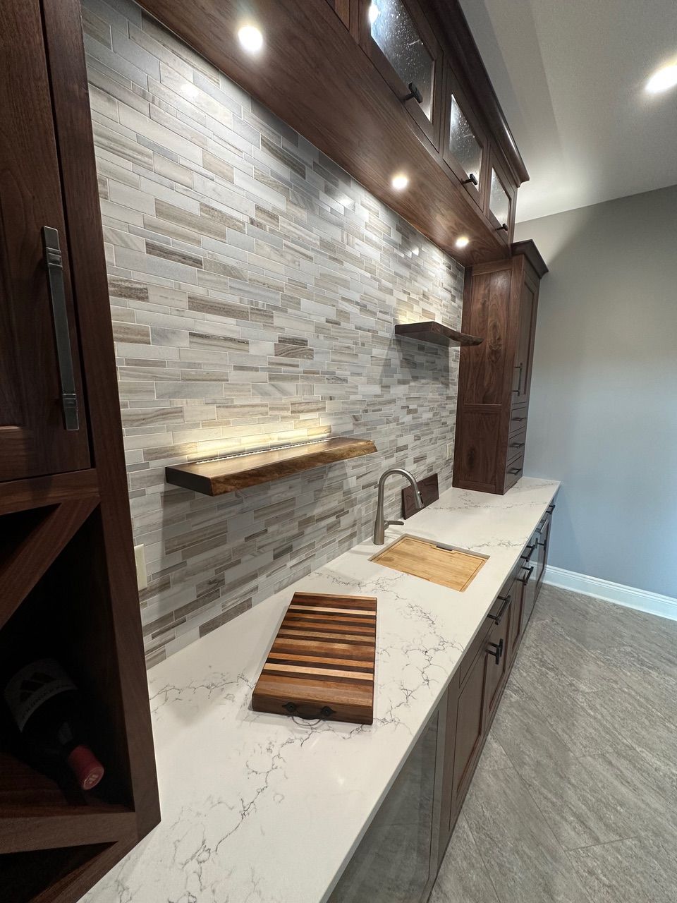 A home bar with a stone tile backsplash, wood shelves and cabinetry, a white countertop, and a built-in sink.